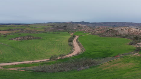 Dirt-road-aerial-shot-between-green-fields-pasture-Spain-cloudy-day